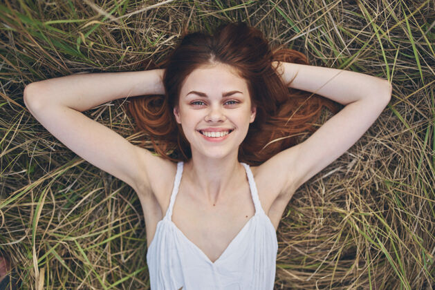 光快乐的女人穿着白色的衣服躺在户外的干草里 用手做手势触摸日落年轻