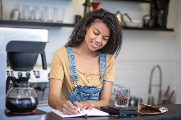 家具会计 咖啡馆漂亮年轻的黑白混血女在咖啡馆吧台的笔记本上写着咖啡的重量外观自营职业咖啡