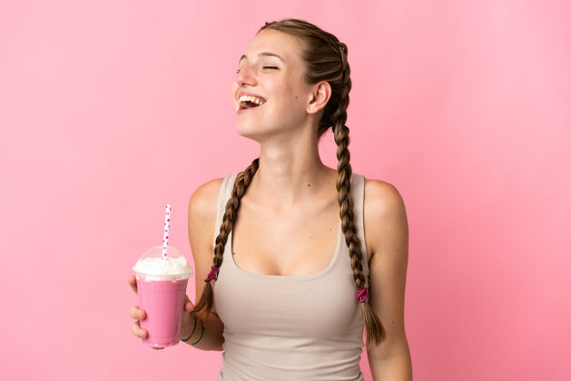 表情一个拿着草莓奶昔的年轻女人站在粉色背景上笑着年轻大笑女性