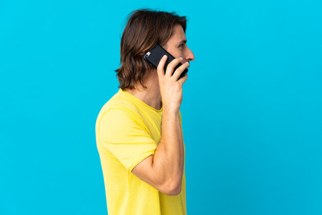 彩色年轻帅哥孤零零地站在蓝色的墙上 用手机和别人聊天瘦身长发手机