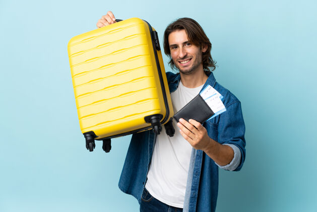 身份证年轻帅哥带着手提箱和护照被隔离在蓝色的墙上度假包人男人