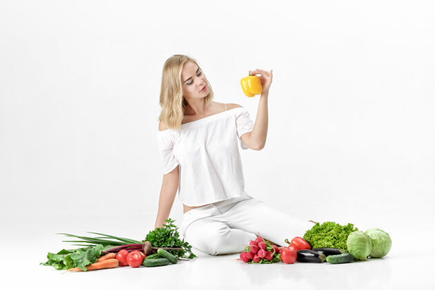 漂亮漂亮的金发女人 穿着白衣服 白色的桌子上放着很多新鲜蔬菜背景女孩拿着甜椒有机蔬菜胡萝卜