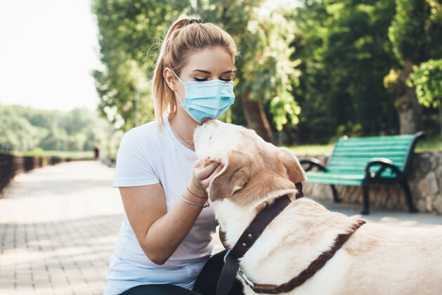 冠状病毒可爱的金发女孩和她的拉布拉多犬在公园里拥抱 戴着医用面具兽医消毒剂面具