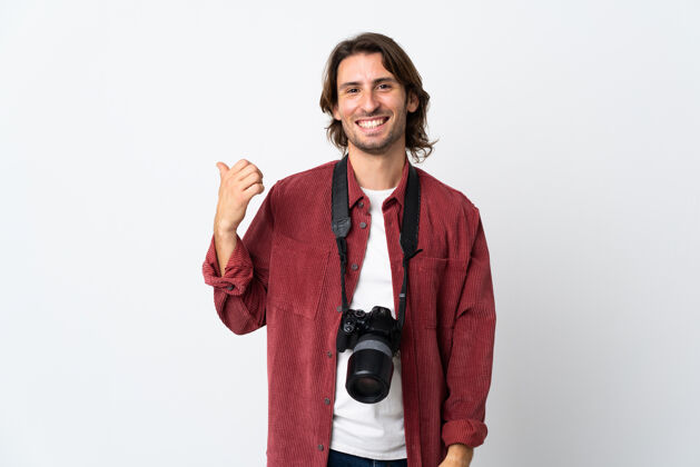 看年轻的摄影师孤立地站在白色的墙上指着旁边展示一个产品设备人男