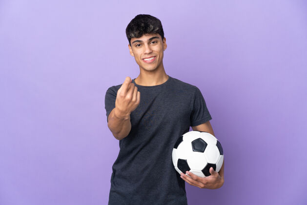 足球一个年轻的足球运动员越过隔离的紫色墙壁做着即将到来的手势男性运动装足球