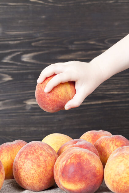 件大量新鲜柔软的桃子放在亚麻桌布上 特写 其中一个桃子被一个孩子捡了起来烹饪桌布甜