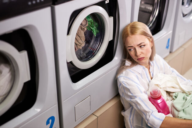 家务疲惫的女人坐在洗衣机旁抬头看可悲的是 白种人女人把时间花在洗衣服上 等着 把脏衣服放在篮子里让女人厌烦抑郁家庭洗衣