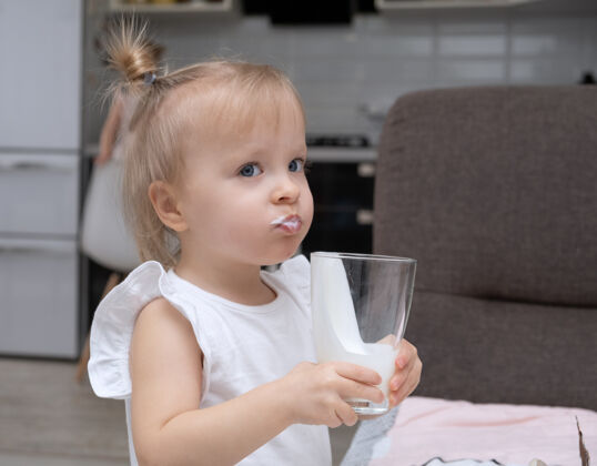 奶制品可爱的金发小女孩喝着有机牛奶 在家里的厨房里拿着玻璃杯餐饮牛奶饮料