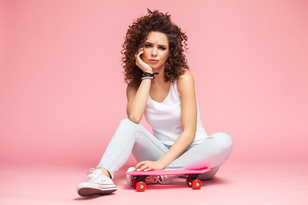 发型快乐迷人的年轻女子坐在粉红色的滑板上享受滑板女人