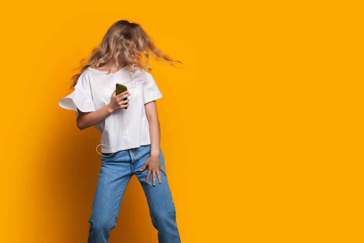 女性金发女郎拿着一部手机在一间黄色工作室的墙上跳舞 旁边有免费的广告空间快乐室内休闲