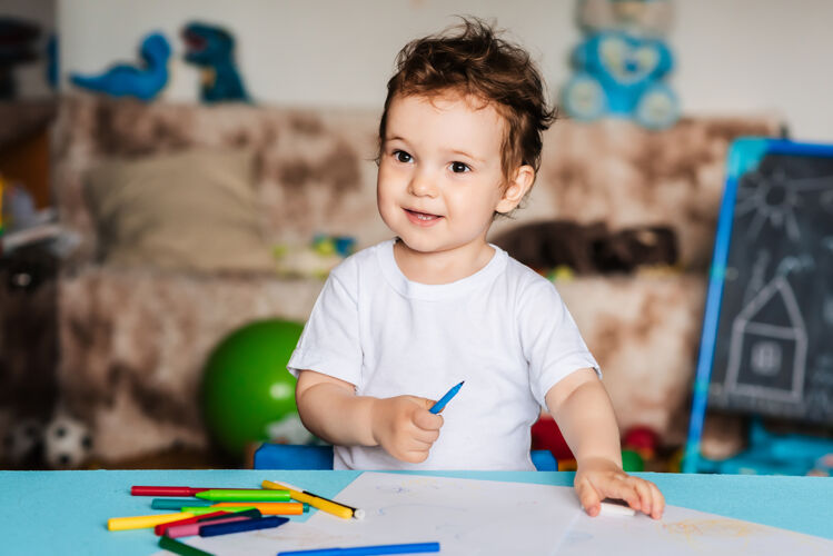 学习一个小男孩用彩色铅笔在桌子上的一张纸上画画童年绘画小学