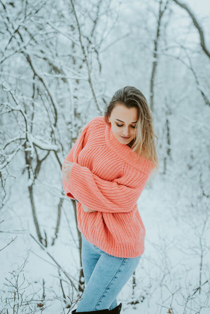 年轻一个穿着粉色宽松毛衣和牛仔裤的漂亮女孩在寒冷的雪域森林里享受性感新鲜