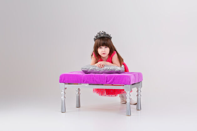 头发穿着粉色公主裙 头戴皇冠 坐在灰色的粉色椅子上的漂亮的小黑发女孩背景可爱宝贝背景漂亮灰色