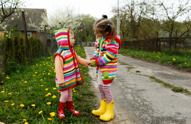 户外两个穿着鲜艳衣服的小女孩在黄色的树林里互相握着手蒲公英快乐童年手自然放松