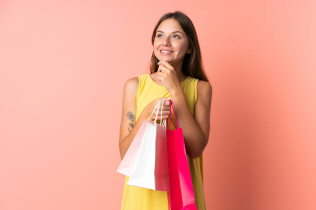 成人一位年轻的立陶宛妇女 手拿购物袋 在粉红色的背景下孤独地思考着销售粉色容器