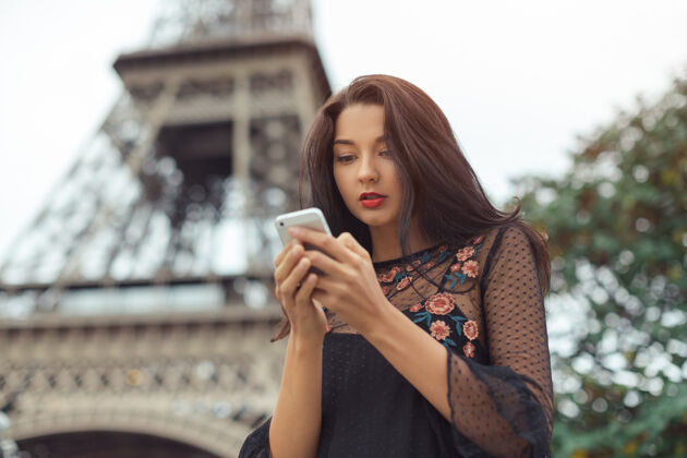 埃菲尔铁塔快乐旅行的女人在埃菲尔铁塔和旋转木马附近使用智能手机 巴黎肖像旅行的乐趣服饰旅游城市景观