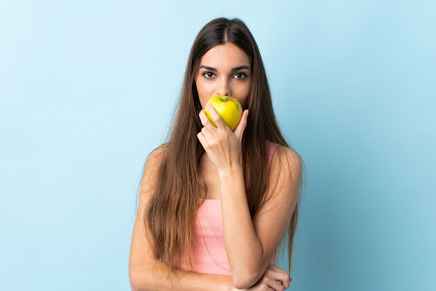女性一个年轻的白人妇女在蓝色背景下吃苹果饮食美味健康