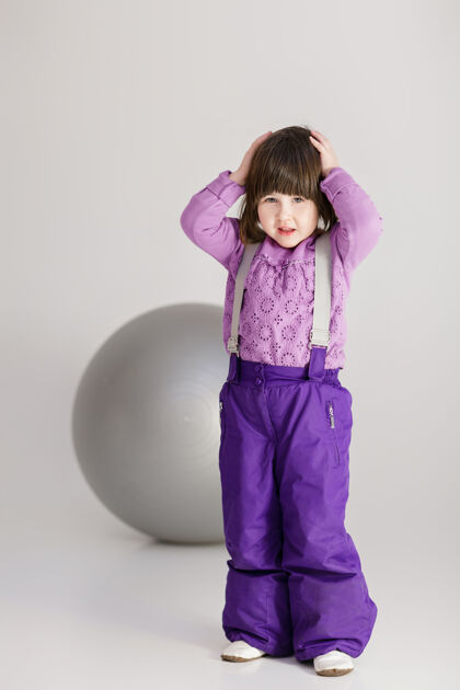 休闲穿着紫色衣服的可爱小女孩抱着他的头 在灰色背景上健身用的大球放松年轻大