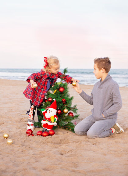 男孩哥哥和妹妹在海滩上装饰圣诞树装饰童年家庭