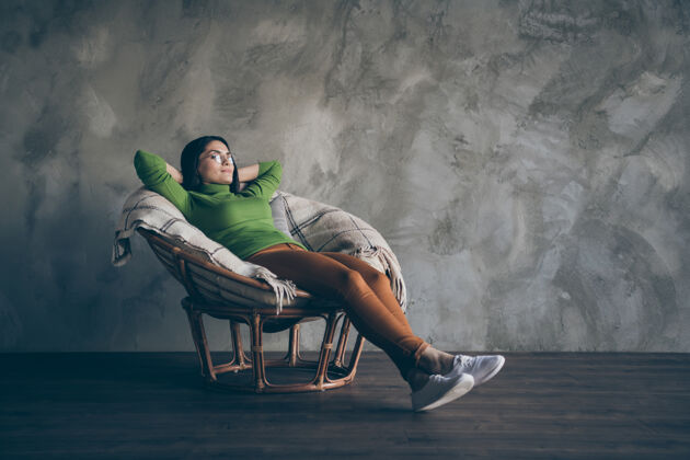 工人全身尺寸的照片 欢快的商务女士躺在扶手椅上休息 穿着橙色裤子 隔着灰色墙壁混凝土背景 远远望着窗外冷静休息计划