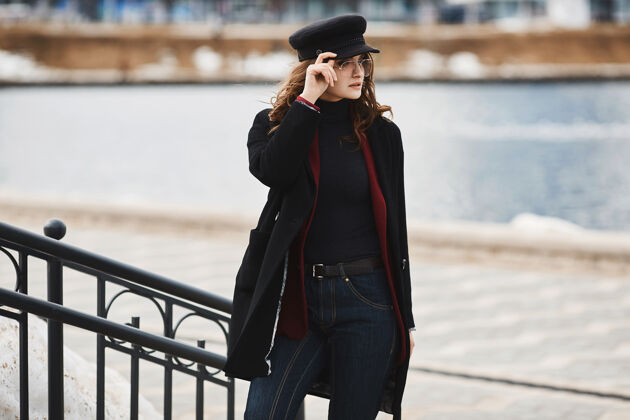 外套穿着外套 戴着时髦帽子 戴着太阳镜的时髦年轻女子在城市背景下摆姿势摩登生活方式Fashion