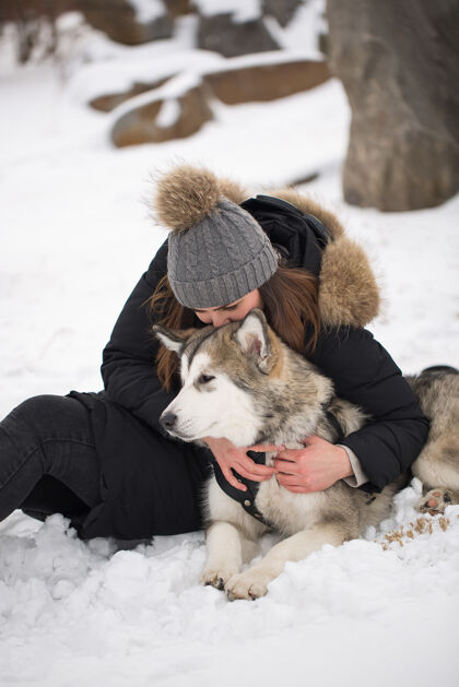 松树冬天森林里美丽的女孩狗玩和狗西伯利亚哈士奇夹克女孩在一起