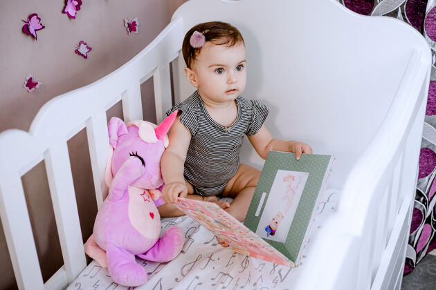 相册惊喜 可爱的宝宝打开她的相册在婴儿床上 看着她的妈妈仔细可爱室内房间