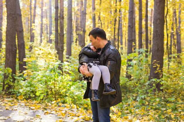 年轻父亲 家庭和休闲的概念-父亲抱着小女儿在秋季公园女孩爸爸快乐