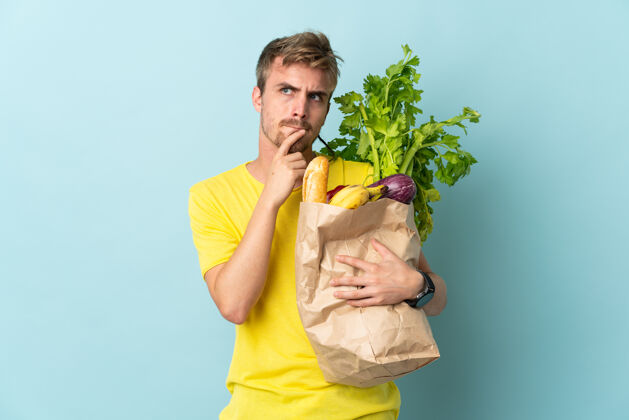 青年一个金发碧眼的人拿着一袋外卖食品孤零零地对蓝色有着怀疑和思考有机蔬菜人