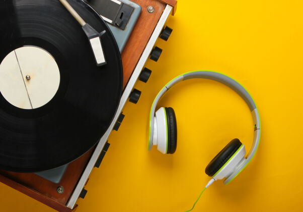 播放复古乙烯基唱片播放器与立体声耳机的黄色表面电子播放设备