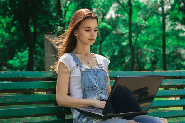 电脑迷人的黑发女郎坐在长凳上 手里拿着一台笔记本电脑书聊天便携式