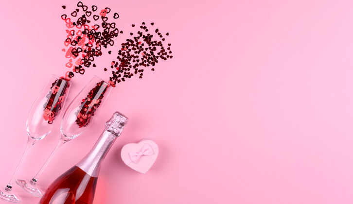 礼物两个装满心形亮片的香槟酒杯 一瓶香槟和一份粉色背景的情人节礼物情人节玻璃杯情侣