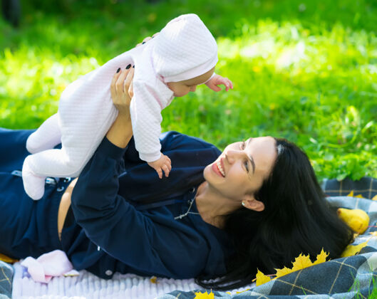女人秋天 一个公园里 可爱的母亲在绿草上躺在毯子上 一边和她的小女孩玩耍 一边把她举到空中 一边笑着封闭可爱举