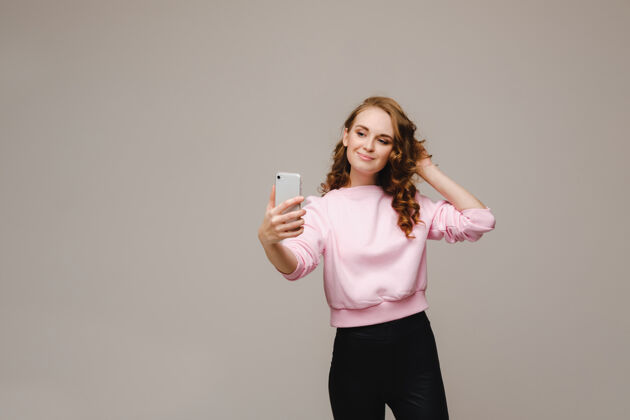 运动一个微笑的快乐女孩穿着粉色上衣 在灰色的手机上自拍小玩意生活方式休闲