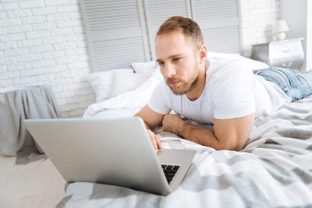 积极性享受我的周末很高兴运动迷人的男人躺在床上 一边用笔记本电脑表达兴趣网络内部发展