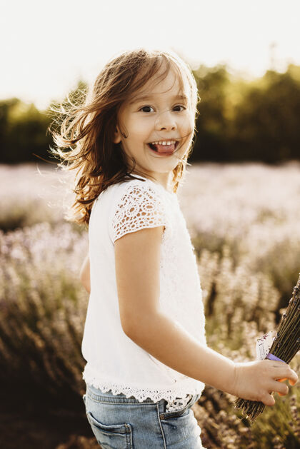 金色可爱的小女孩看着镜头微笑着在一片薰衣草地里对着日落秀舌头农业日出户外