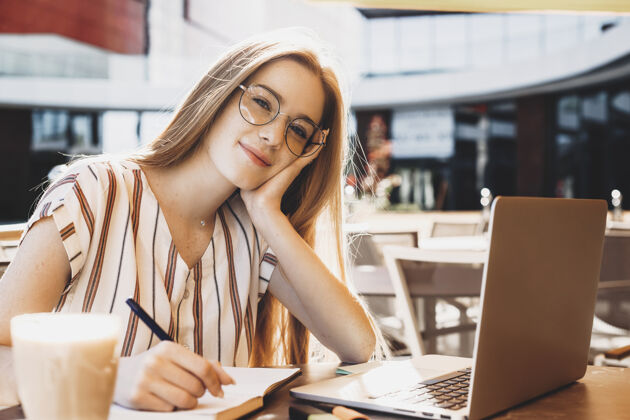 沟通一位红发雀斑的迷人年轻女子的肖像 一边看着相机 一边在外面喝咖啡 一边在笔记本电脑前工作休闲笔记本电脑电脑