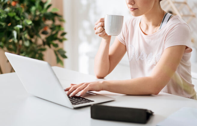 笔记本电脑寻找一个解决方案不错轻松但专注的女孩使用她的电脑浏览一些网页 而上午喝咖啡女人自营职业明亮