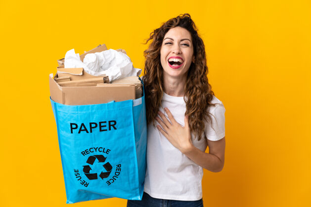 积极年轻女子手里拿着一个装满废纸的回收袋 对着黄色的孤零零笑了很多志愿者生态脸