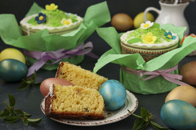 美味静物画用彩纸做的复活节蛋糕和深色表面上的彩色复活节彩蛋 在前景中切块的复活节蛋糕 特写大季节霜冻