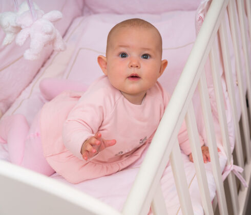 装饰警惕好奇的小女婴在婴儿床上看着相机在一个特写镜头惊奇信任保姆护理