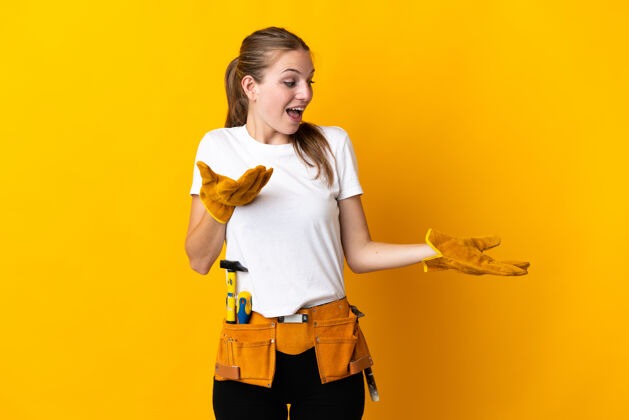 女人年轻的电工女人被隔离在黄色背景下 脸上露出惊讶的表情技能工具手势