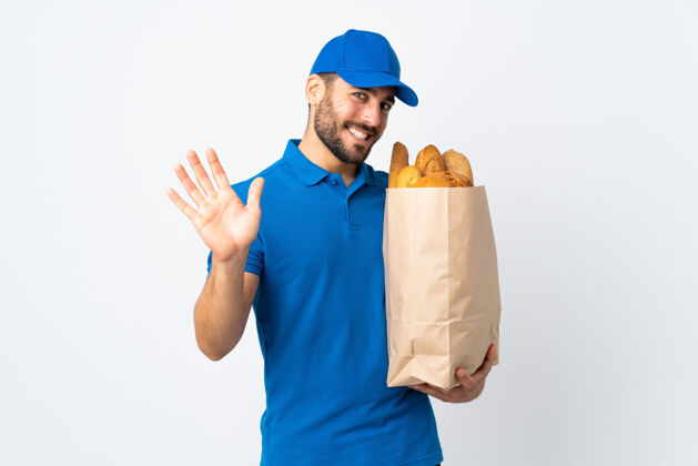 面包送货员拿着一袋面包 孤立地站在白色的背景上 带着幸福的表情用手敬礼敬礼厨房胡须