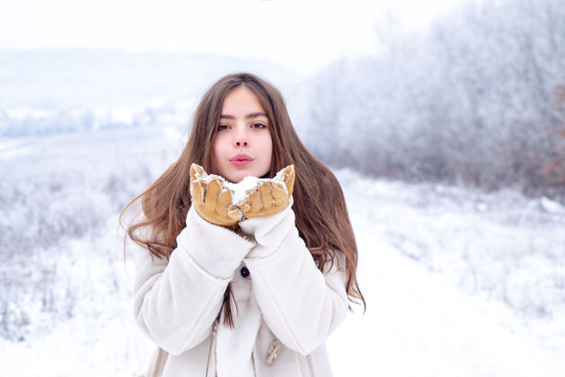活动爱冬天快乐吹着红唇的酷女孩穿着雪地背景上的白色毛衣做空中接吻假期自然雪