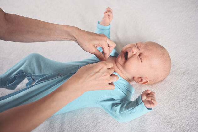 甜蜜妈妈穿着可爱的情绪有趣的新生小男婴在蓝色连体衣打扮医学男孩