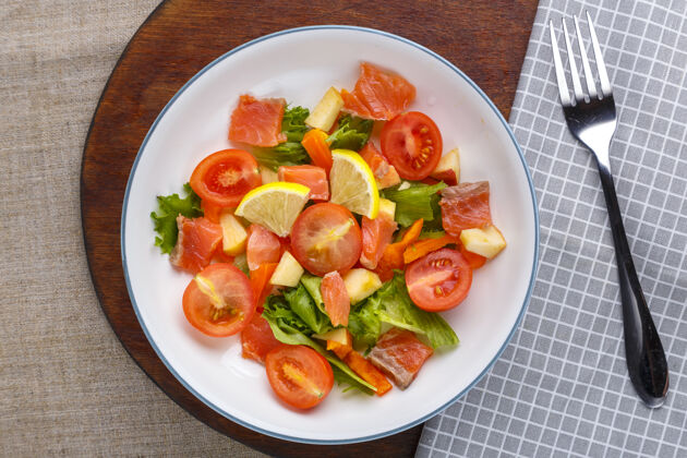 樱桃番茄在一个灰色的盘子里放一个凉拌三文鱼和樱桃西红柿沙拉 放在一个木头架子上叉子旁边的架子上新鲜番茄健康