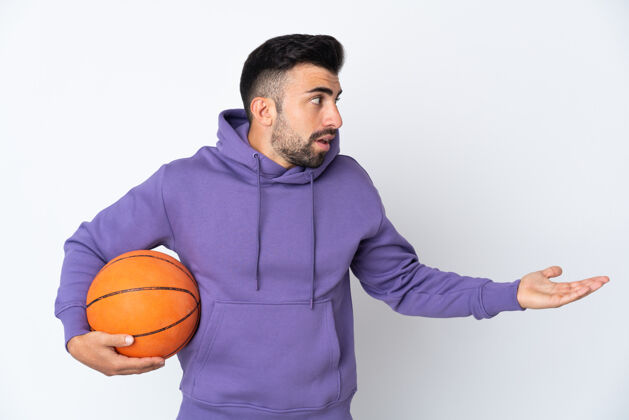 篮球一边看一边在孤立的白墙上打篮球的男人 脸上露出惊讶的表情健身手势成人