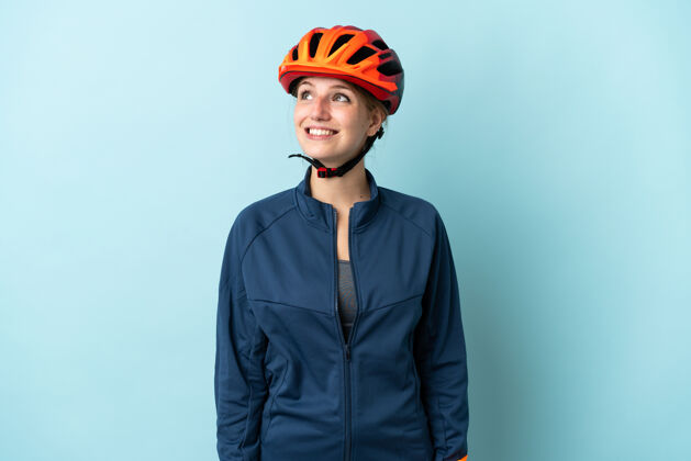 年轻一个年轻的骑自行车的女人被隔离在蓝色的背景下 一边抬头一边思考着一个想法肖像女孩成人