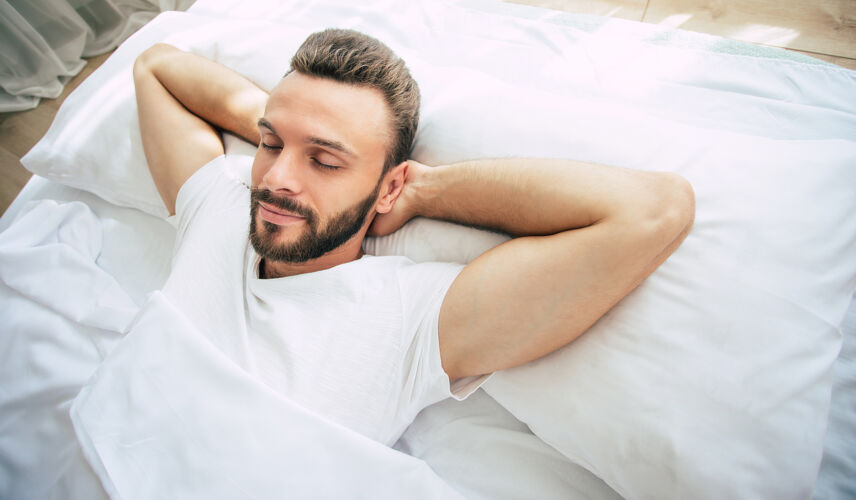 宁静帅气的留着胡子的年轻人睡在舒适的卧室里的白色大床上休息房子卧室