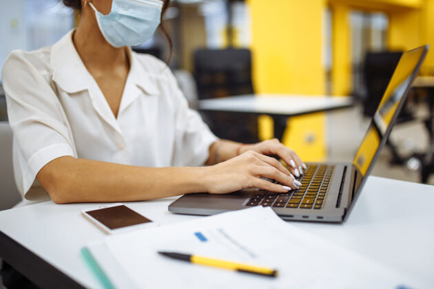 男性一位妇女在办公桌上用笔记本电脑工作 戴着医用口罩 在covid-19大流行期间保持安全预防工作穿着